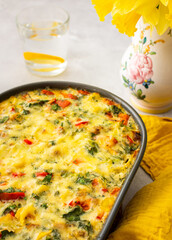 Delicious healthy vegetable pie with broccoli and cauliflower, tomatoes and sweet peppers and cheese in a ceramic dish, daffodils in a vase