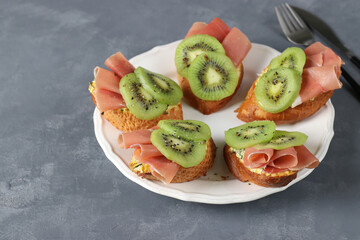 Sandwiches with soft cheese, jamon and kiwi on a white plate. Delicious and healthy breakfast