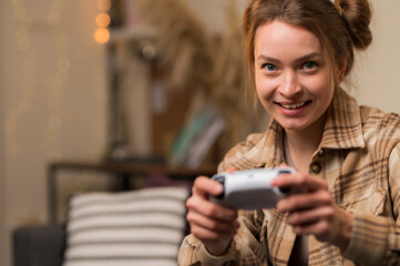 A fair-haired girl gamer with a joystick plays a video game at home, in a room. Close-up. Virtual reality, recreation, entertainment, holidays, communications, fun adventure video games with friends.