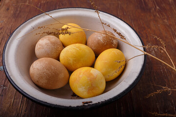 Bowl of painted Easter eggs. on wooden brown table with dry branch. Yellow and brown colored Easter eggs. Close up shot