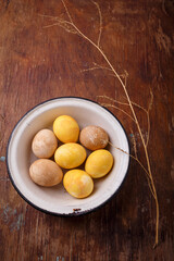 Yellow and brown Easter eggs in white bowl on wooden table. Top view, copy space, vertical shot