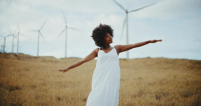 Happy young black woman in golden field with windmills on mountain side, clean energy, sustainability, and diversity, fighting climate change