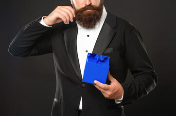 cropped man in tuxedo bow tie on black background with business reward box. occasion greeting.