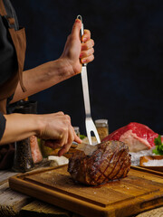 Cooking ham by the hands of a professional chef on a wooden kitchen table on a dark blue...