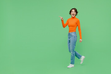 Full body young smiling happy cool fun woman 20s wearing casual orange turtleneck walk going point...