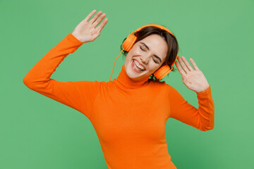Young smiling happy woman 20s wear casual orange turtleneck headohones listen to music dance have...