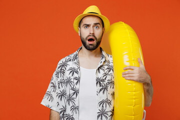 Young dissatisfied shocked tourist man wear beach shirt hat hold inflatable ring travel abroad on weekends isolated on plain orange background studio portrait Summer vacation sea rest sun tan concept - obrazy, fototapety, plakaty