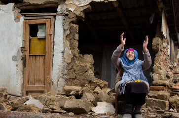 A woman prays in front of a destroyed house during the war. Ukrainian woman on the ruins of a war-torn house. War in Ukraine. Bombardment of Ukrainian cities. Ukrainian refugees.