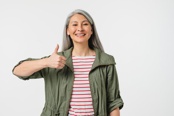 Positive smiling happy mature middle-aged woman with grey hair showing thumb up looking at camera...