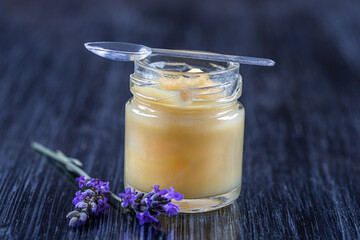 Close up of a jar of royal jelly covered with a spoon with sprigs.