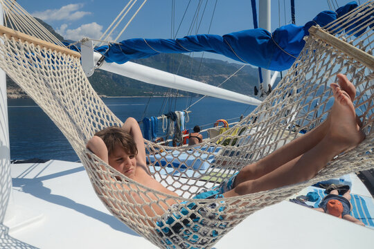 Boy is lying in a hammock on the deck of a yacht at sea on a sunny summer day. Mediterranean Sea, Turkey.