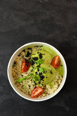 Bowl with bulgur, tomatoes, chicken meatballs and broccoli sauce in eco paper container on black background. Healthy food delivery service and daily ration concept.