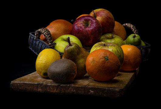 Still life of mixed fruit on wooden cutting board with basket