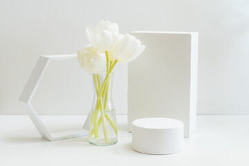 Geometric podium or pedestal with white spring tulips in a vase on a white background. Empty podium...