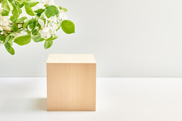 Empty square wooden podium for product presentation and spring flowers on a light background. Mockup concept with copy space