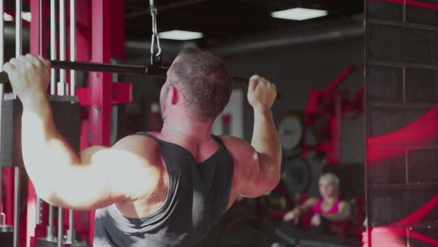 Back view of an attractive man bodybuilder performing Lat pulldown at gym