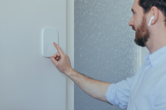 Businessman enters finger password lock code on alarm panel, on white wall, rear view of man with beard