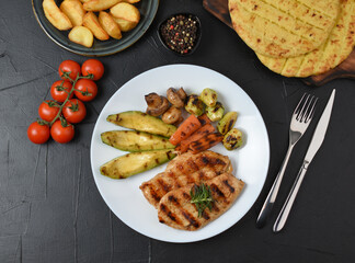 Grilled chicken steak fried potatoes and vegetables on dark background