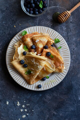 Crepes with honey, mint leaves, blueberries on gray stone background. close up with copyspace. Delicious crepes, thin pancakes