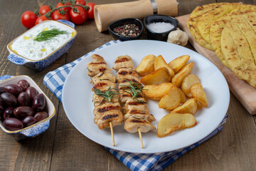 Fried souvlaki, pita and Greek tzatziki with potatoes on wooden table. Appetizing kebab on wooden sticks.