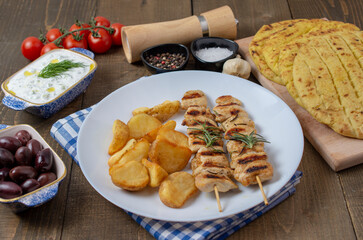 Grilled meat skewers on a wooden table with vegetables and potatoes. Greek meal with tzatziki and olives