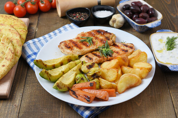 Tasty fresh meal with grilled chicken with potatoes, avocado, mushrooms, carrots in white bowl on wooden  background. Olives, pita, tomatoes and tzatziki. Diet Keto Paleo Concept. 