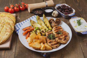 Tasty fresh meal with grilled chicken with potatoes, avocado, mushrooms, carrots in white bowl on wooden  background. Olives, pita, tomatoes and tzatziki. Diet Keto Paleo Concept. 