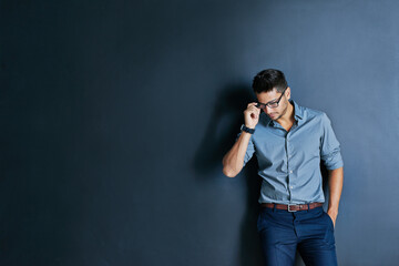 Looking sharp everyday. Studio shot of a focused young man wearing glasses while standing with one hand in his pocket and looking down.