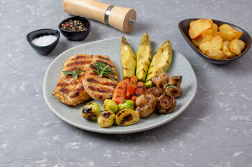 Grilled chicken steak fried potatoes and vegetables on grey background
