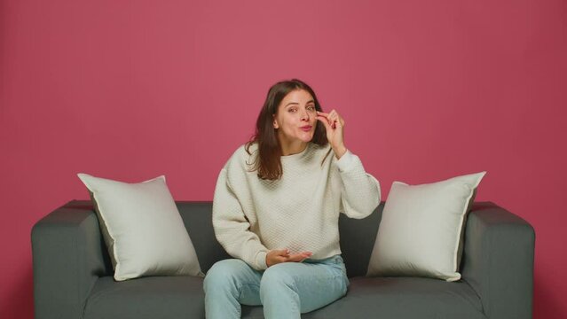 Smiling young girl shows little size gesture by fingers, sitting on sofa. Small prices, sale, discounts in online store