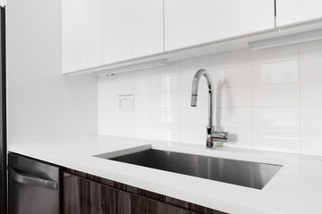 A detail shot of a kitchen sink with white and wood modern cabinets, chrome faucet, and subway tile...