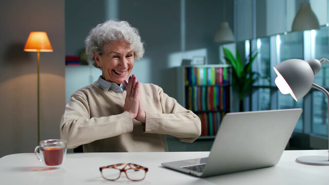 Happy elderly woman using laptop and smiling sitting in spacious living room at home