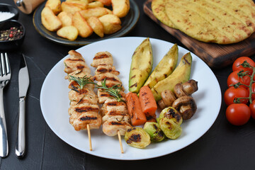 Fried souvlaki with pita, greek salad, potatoes, cherry tomatoes, olives and tzatziki, with variety of spices on dark background. 