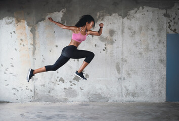 Fototapeta na wymiar Springing back into action. Full length shot of an athletic young sportswoman jumping in the air against a wall outdoors.