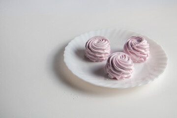 There are three pink marshmallows in a plate on the table. On a white background.
