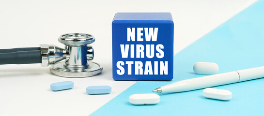 On a white and blue surface are pills, a stethoscope, a pen and a cube with the inscription - new virus strain