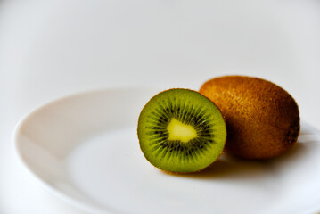 A whole kiwi fruit and half on a white plate