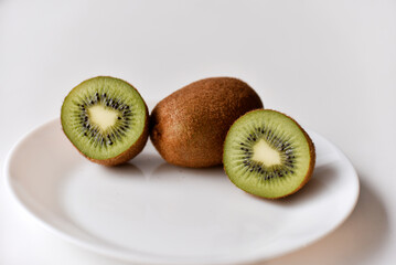 A whole kiwi fruit and half on a white plate