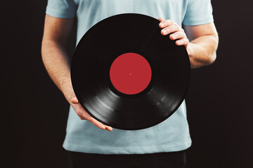 Man with vinyl record. Vintage music style. Male wearing blue t-shirt holding black analog disk standing on black background. Retro music