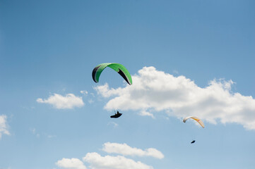 Two paragliders flying in the blue sky against the background of clouds. Paragliding in the sky on a sunny day.