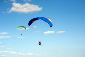 Two paragliders flying in the blue sky against the background of clouds. Paragliding in the sky on a sunny day.