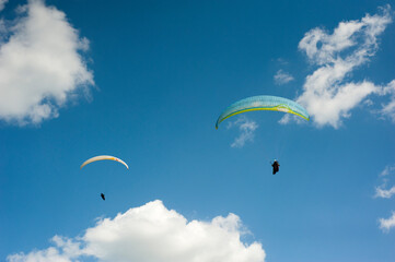 Two paragliders flying in the blue sky against the background of clouds. Paragliding in the sky on a sunny day.