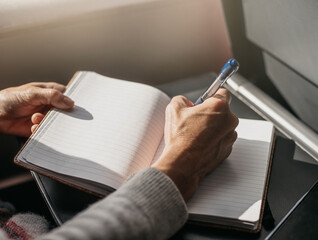 a person writes in a diary on a train while traveling. the soft light comes in through the window. work and travel concept. © Karlos Garciapons