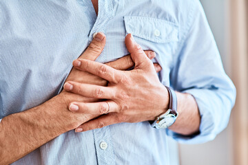Chest pains are never a good sign. Shot of a unrecognizable man holding his chest in discomfort due to pain at home during the day. - Powered by Adobe