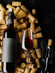On a black background there are a lot of wine corks, a bottle of red wine, a corkscrew and a wine...