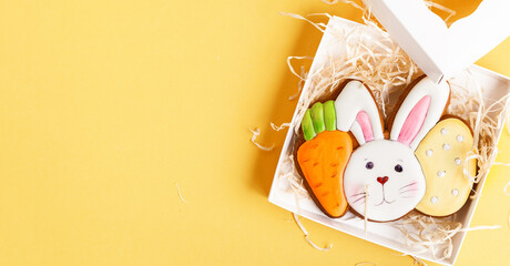 Gingerbread cookie in the shape of rabbit head with carrot and egg. Easter bunny cookie in the gift box on the yellow background.