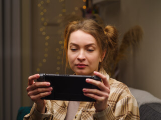 A pretty girl is playing a mobile game on a portable game console in the room. Passion, recreation,...