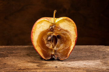 A rotten moldy apple, decomposing, on an wooden shelf. Close-up.