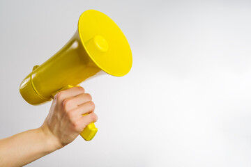 A man's hand holds a yellow loudspeaker, megaphone. Isolated on white background. It symbolizes untrue news, rumors, fakes, accusations, yellow press. Advertising, banner.