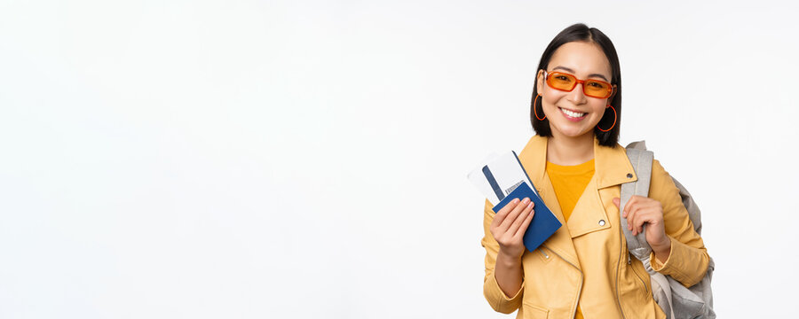 Happy asian girl going on vacation, holding passport and flight tickets, backpack on shoulder. Young woman tourist travelling abroad, standing over white background
